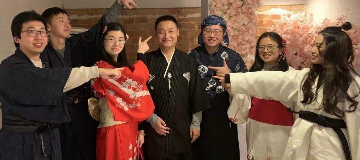 Un groupe de 3 jeunes joueuses et 3 jeunes joueurs, en habits traditionnels chinois, menacent en souriant une septième personne de leurs doigts en faisant le signe du pistolet.