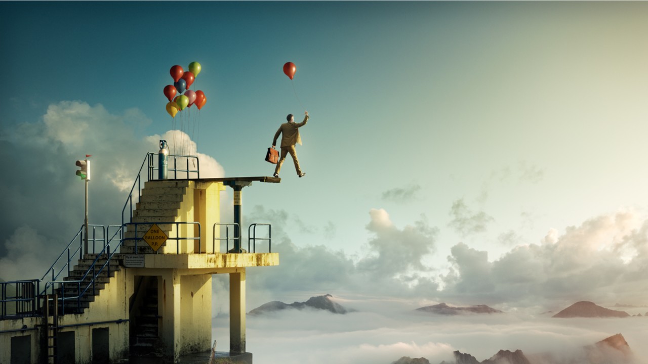 Un homme sur le point de marcher hors de la planche d'un plongeoir, tenant un petit ballon gonflé à l'hélium.