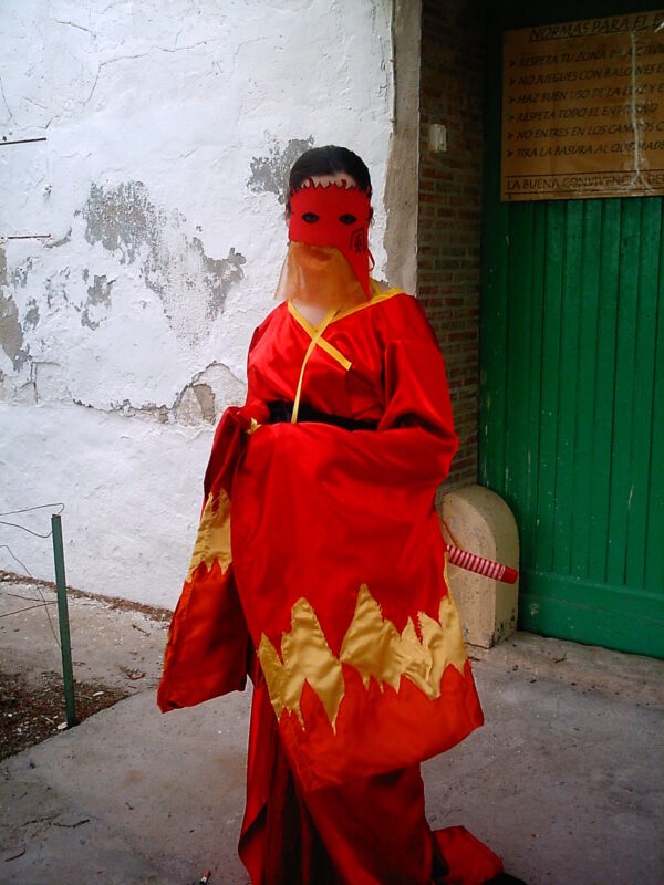 Photo de l'autrice déguisée : masque et kimono rouges et or, avec une katana, tel que décrit dans les livres sur le Clan du Scorpion dans L5A.