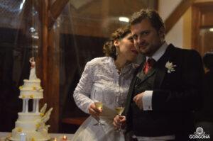 Photo d'une scène de mariage : pièce montée, mariée en blanc qui chuchotte joyeusement à l'oreille du marié en costume pendant qu'iels portent un toast avec des flutes de champagne.