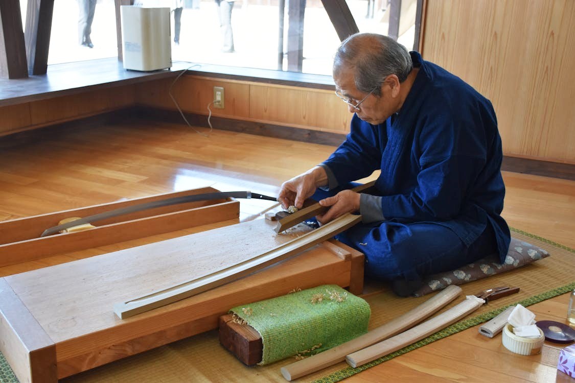 Photo d'un vieil artisan japonais rabottant d'un air blasé un étui en bois pour les épées.